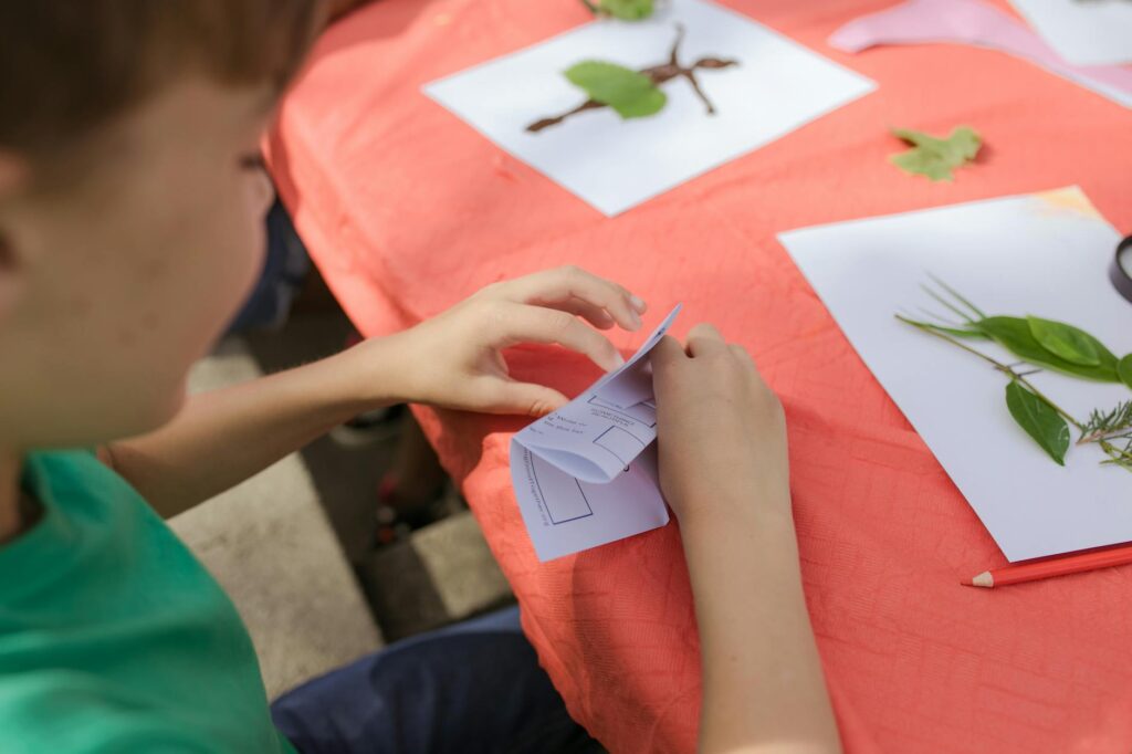 A child participates in a nature-themed craft project at an outdoor camp, creating with leaves.