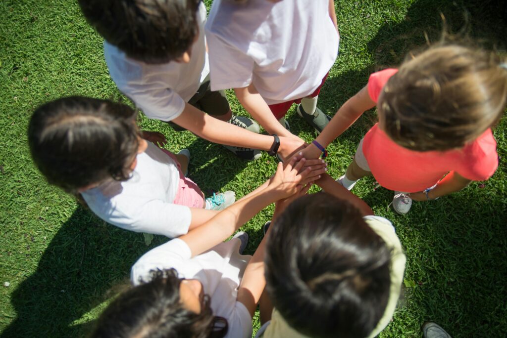 Top-view of children joining hands as a team in a sunny park, promoting unity.